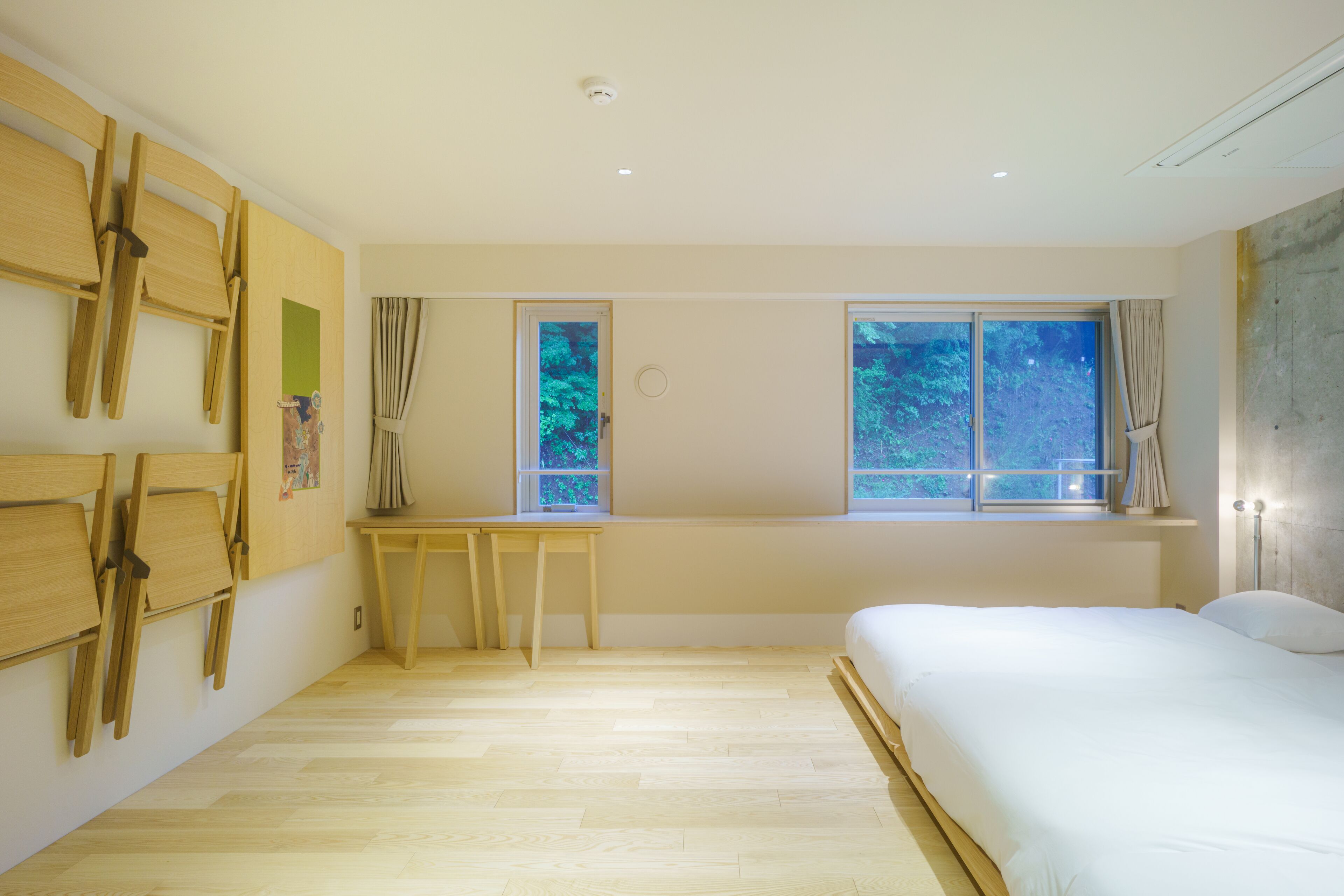A bedroom with a bed, wooden chairs, a desk, and windows with curtains.