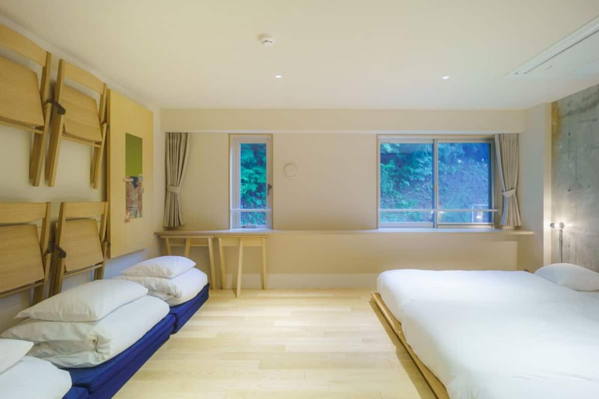 A room with two beds, a desk, and a window with a view of trees.