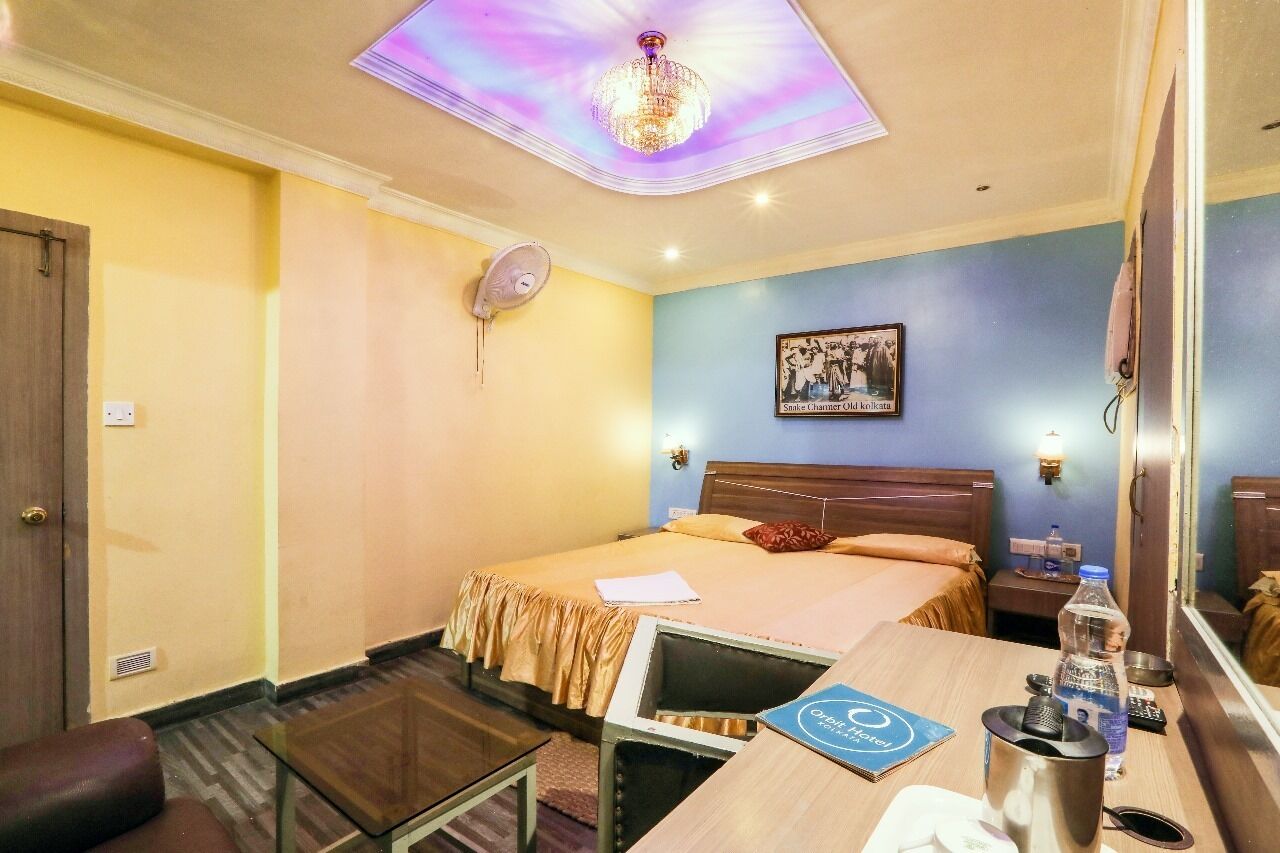 A hotel room with a bed, bedside table, chair, and a ceiling light fixture.