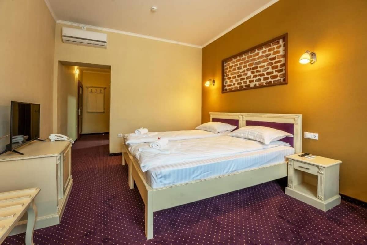 Habitación de hotel con cama, escritorio, silla, televisor y lámpara de pared.