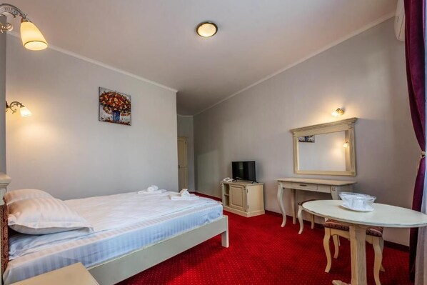 Una habitación de hotel con cama, escritorio, silla, televisor y espejo.