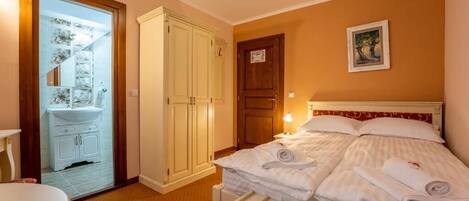 A hotel room with a bed, a bedside table, a wardrobe, and a bathroom visible through a glass door.