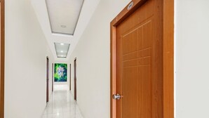 Un pasillo con una puerta de madera a la derecha, piso de baldosas y un cuadro verde en la pared.