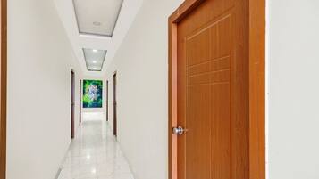 A hallway with a wooden door on the right, a tiled floor, and a green painting on the wall.