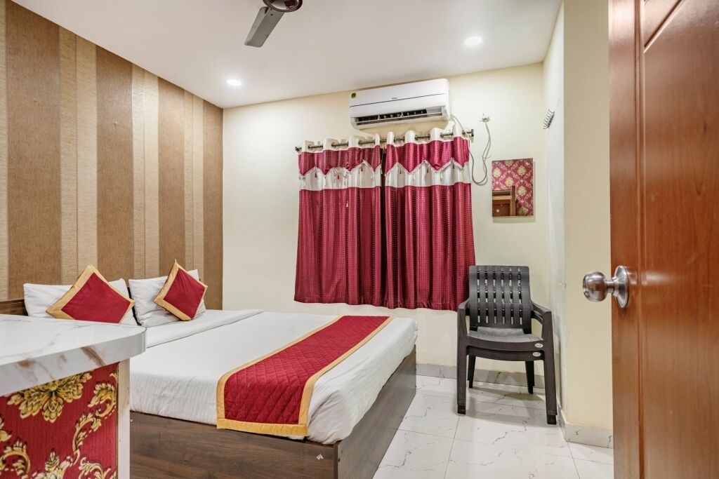 A hotel room with a bed, a chair, an air conditioning unit, and a curtain.