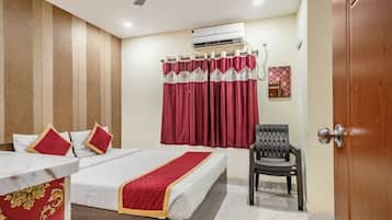 A hotel room with a bed, a chair, an air conditioning unit, and a curtain.