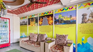 Un vestíbulo de hotel con un refrigerador rojo de Coca-Cola, un sofá con cojines estampados y paredes decoradas con carteles coloridos de lugares emblemáticos.