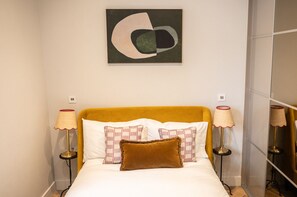 Un lit avec une tête de lit jaune, deux lampes de chevet et un tableau abstrait accroché au mur.
