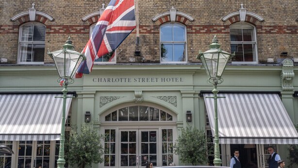 Het uiterlijk van het Charlotte Street Hotel, met een opvallende Britse vlag, klassieke architectuur en een gestreepte luifel.
