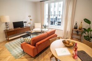 Ein modernes Wohnzimmer mit einer Couch, einem Esstisch, einem Fernseher und einem Fenster mit Vorhängen.