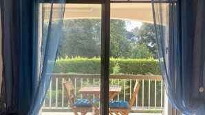 Una puerta corrediza de vidrio con cortinas azules, que da a una terraza exterior con una mesa de madera y dos sillas.