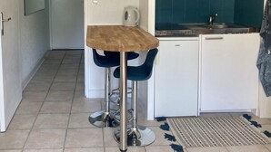 Una cocina compacta con un refrigerador blanco, un microondas y un lavabo. Hay una mesa de madera con dos sillas azules.