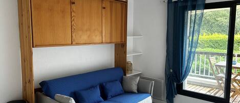 A room with a sofa, wooden cabinets, a small table, and a view of an outdoor deck.