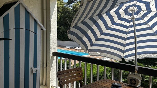 Una terraza de madera con una mesa y sillas, un paraguas a rayas y un cobertizo azul y blanco.