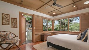 A bedroom with a large bed, wooden flooring, a ceiling fan, and large windows offering a view of greenery. - Fairways South 23 Four Bedroom (Kamuela)