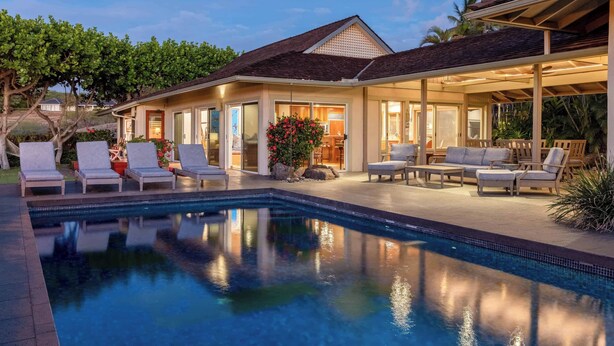 A poolside area with lounge chairs, a covered patio, and a house with large windows. - Fairways South 23 Four Bedroom (Kamuela)