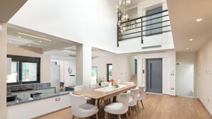 A spacious dining area with a high ceiling, a kitchen with a modern design, and a staircase leading to an upper level. - Elias Rest Villa with private pool (Pastida)