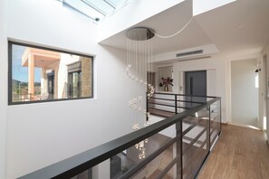 A modern interior with a glass railing, a hanging light fixture, and a view through a large window.