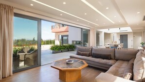 A modern living room with a large sliding glass door leading to an outdoor patio, a sectional sofa, and a wooden coffee table. - Elias Rest Villa with private pool (Pastida)