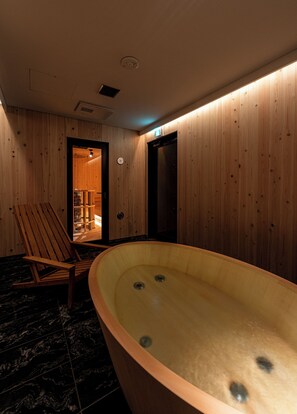 Un interior de madera con una bañera grande, una silla de madera y una puerta que conduce a otra habitación.