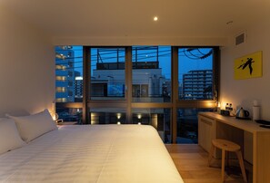A modern hotel room with a large bed, a desk with a stool, and a view of the cityscape through large windows. - 9 HOTEL Tenjin (Fukuoka)