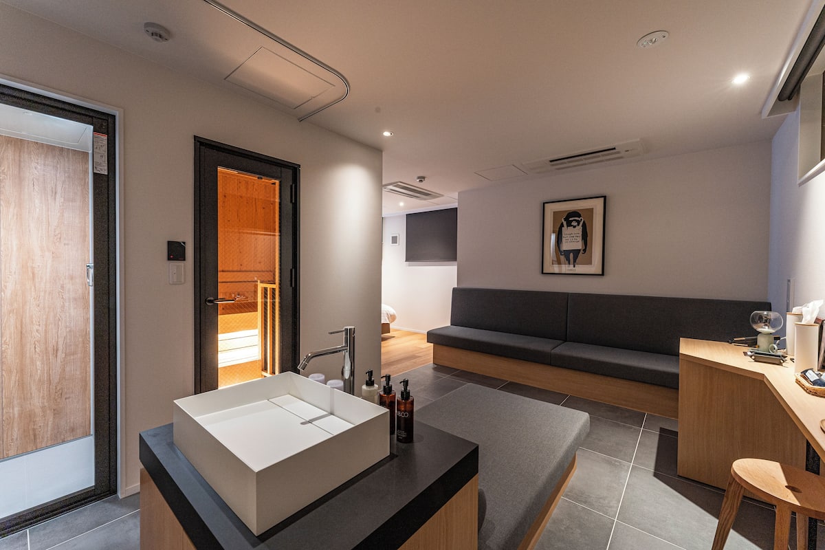 Ein modernes Badezimmer mit einem großen weißen Waschbecken, einer Duschkabine und einer Sitzecke mit Sofa und Schreibtisch.