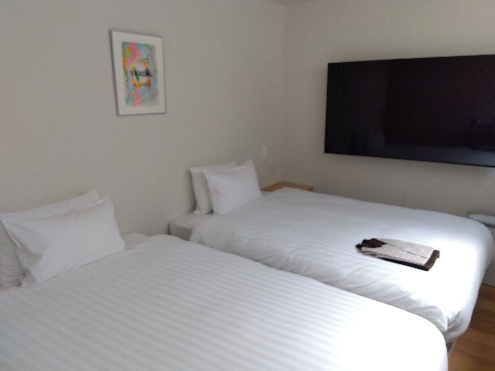 Une chambre d’hôtel avec deux lits, un téléviseur à écran plat fixé au mur et un tableau encadré accroché au mur.