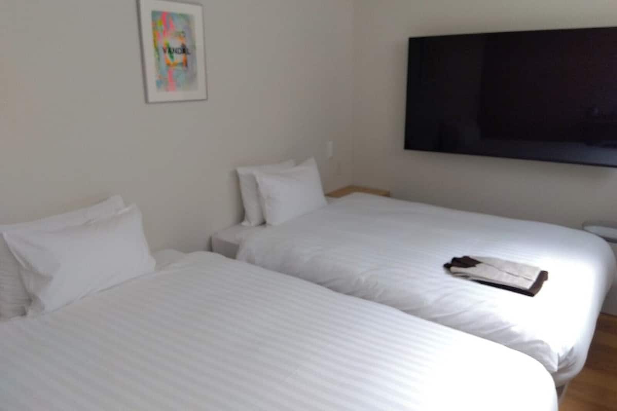 Ein Hotelzimmer mit zwei Betten, einem an der Wand befestigten Flachbildfernseher und einem gerahmten Bild.