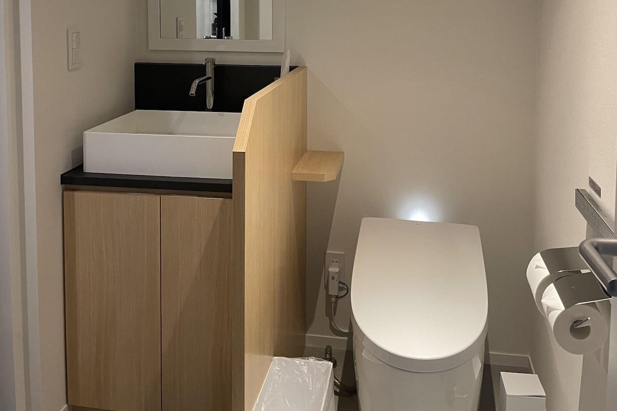 Ein kleines Badezimmer mit einem weißen Waschbecken, einer Toilette und einem Holzschrank.