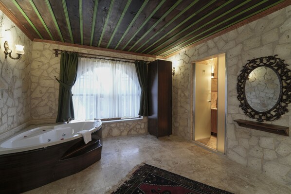 A bathroom with a stone wall, a wooden ceiling, a bathtub, a shower, and a mirror. - By Yüksel Cave Hotel (Ürgüp)