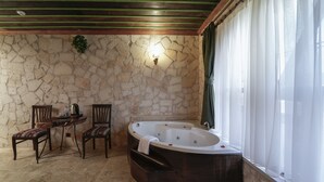 Un baño con paredes de piedra, una bañera independiente, dos sillas de madera y una pequeña mesa con una tetera y tazas.