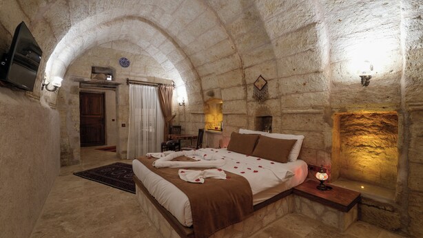 Un dormitorio con paredes de piedra, una cama, una mesita de noche, una lámpara y una chimenea.