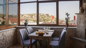 Un rincón comedor con una mesa dispuesta para dos personas, sillas, una planta en maceta y vista a un paisaje rocoso a través de amplias ventanas.