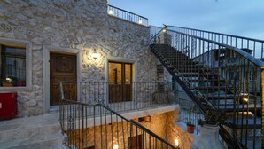 Un edificio de piedra con una escalera que conduce a un segundo piso. Hay dos puertas y un jarrón grande en el segundo piso.