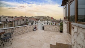 Una terraza en la azotea con muros de piedra, una mesa con sillas y vistas a la ciudad y las colinas al fondo.