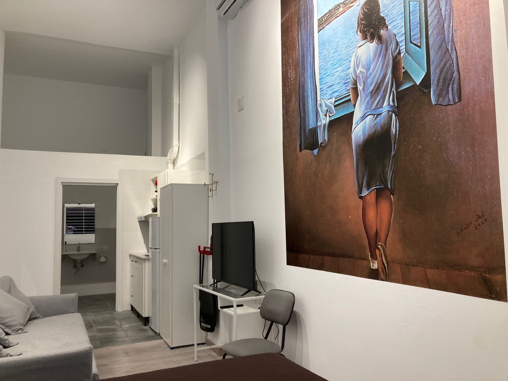 Una habitación moderna con cama, escritorio, silla, televisor y un cuadro grande en la pared.
