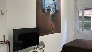 A room with a bed, a desk with a TV, a chair, and a large painting of a woman looking out a window. - Golondrinas de Malaga (Málaga)
