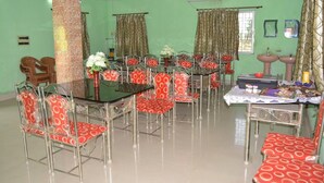 A dining area with a glass-top table and red and white patterned chairs, a brick pillar, and a ceiling fan.