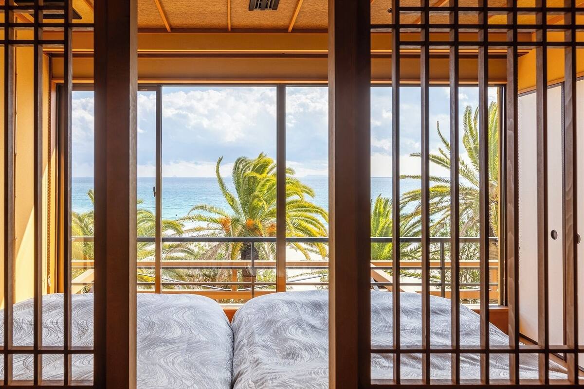 Ein Zimmer mit Blick auf den Ozean, ein Bett mit einem gemusterten Überwurf und eine traditionelle, japanisch gestaltete Schiebetür.