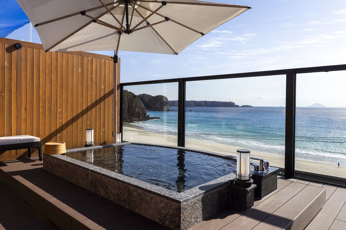Ein Whirlpool mit Holzterrasse, einer Holzwand und Blick auf Strand und Meer.