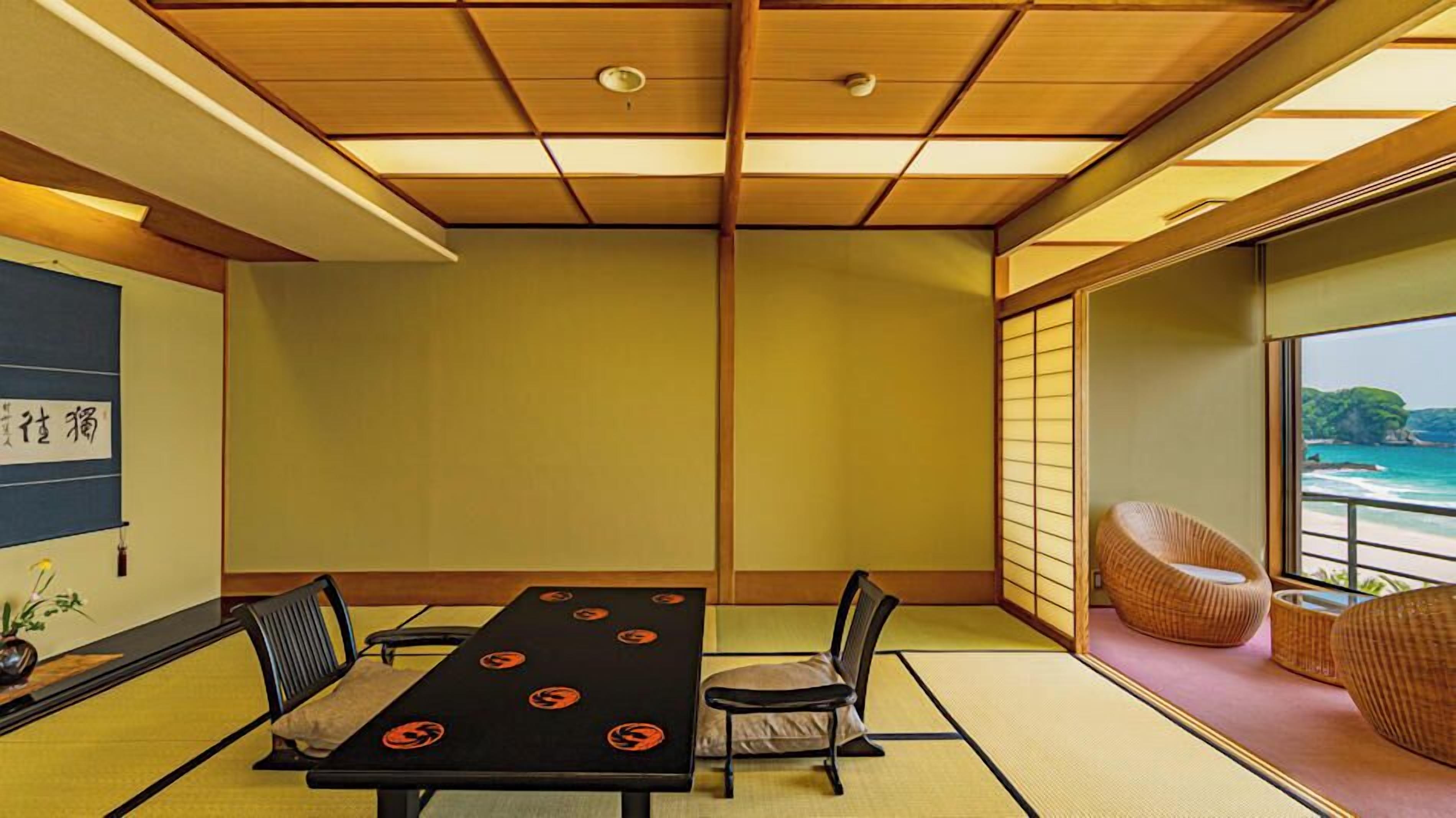 Ein traditioneller japanischer Raum mit Tatami-Böden, einem niedrigen Tisch mit Kissen und Blick auf das Meer durch eine Schiebetür.