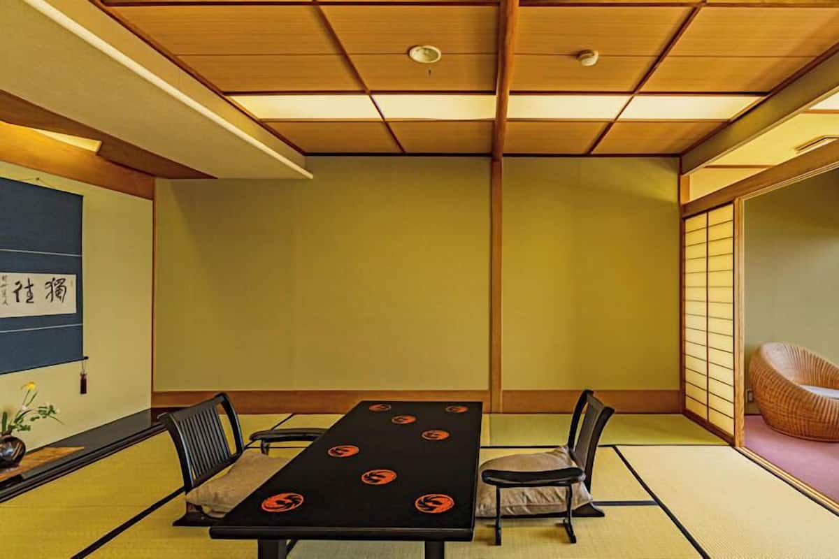 Ett traditionellt japanskt rum med tatamimattor på golvet, ett lågt bord med kuddar och utsikt över havet genom en skjutdörr.