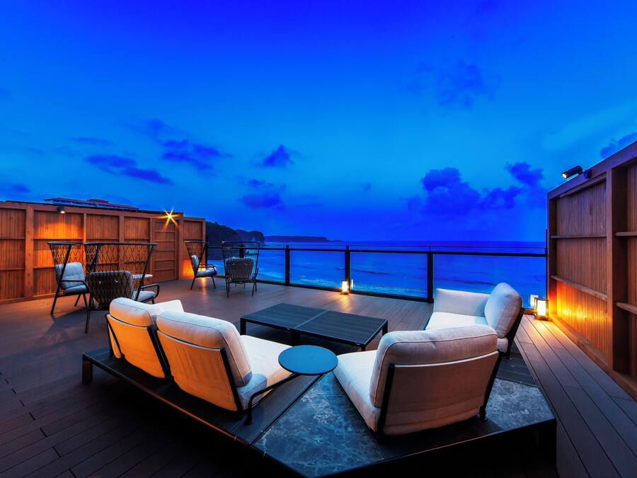 Una terraza con mobiliario exterior y vistas al océano al atardecer.