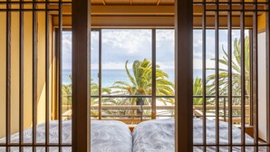 A room with a large window, wooden beams, and a bed with patterned bedding. - izukaorukaze (Shimoda)