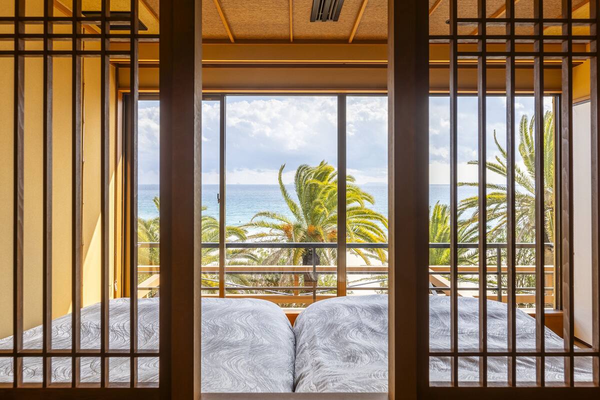 Ein Zimmer mit großem Fenster, Holzbalken und einem Bett mit gemusterten Betttextilien.