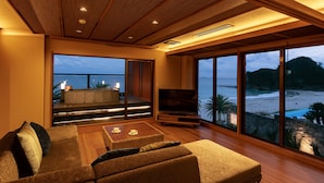 A spacious living area with a large sofa, a coffee table, and a TV. There is a balcony with a view of the beach and ocean. - izukaorukaze (Shimoda)