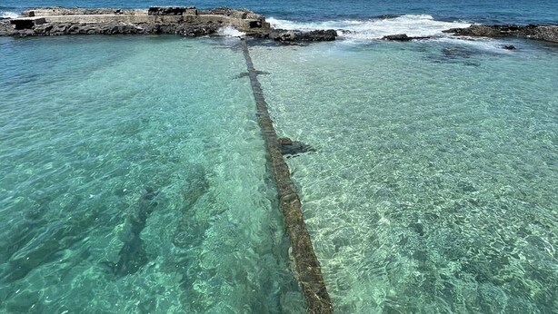 Mare turchese cristallino con l'affioramento di un relitto che si protende nell'acqua.