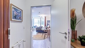 A hallway leading to a living area with a sofa, a table, and a view of the outdoors. - Apartment Rio (Winterberg)