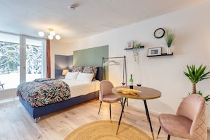 A modern bedroom with a bed, bedside table, chairs, a round table, and a view of snow-covered trees through large windows. - Apartment Rio (Winterberg)