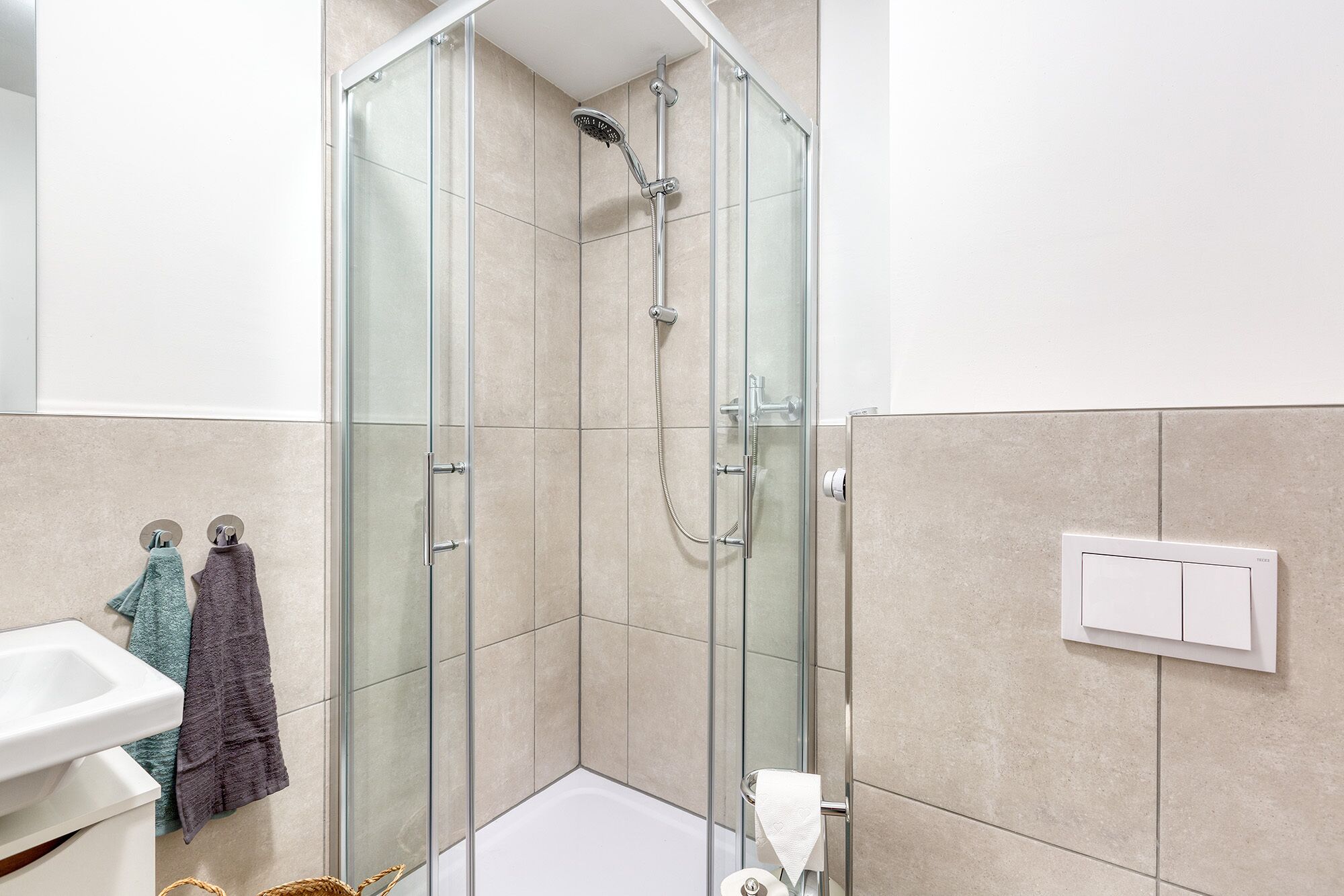 A modern bathroom with a glass-enclosed shower, a white sink, and a towel rack with two towels.